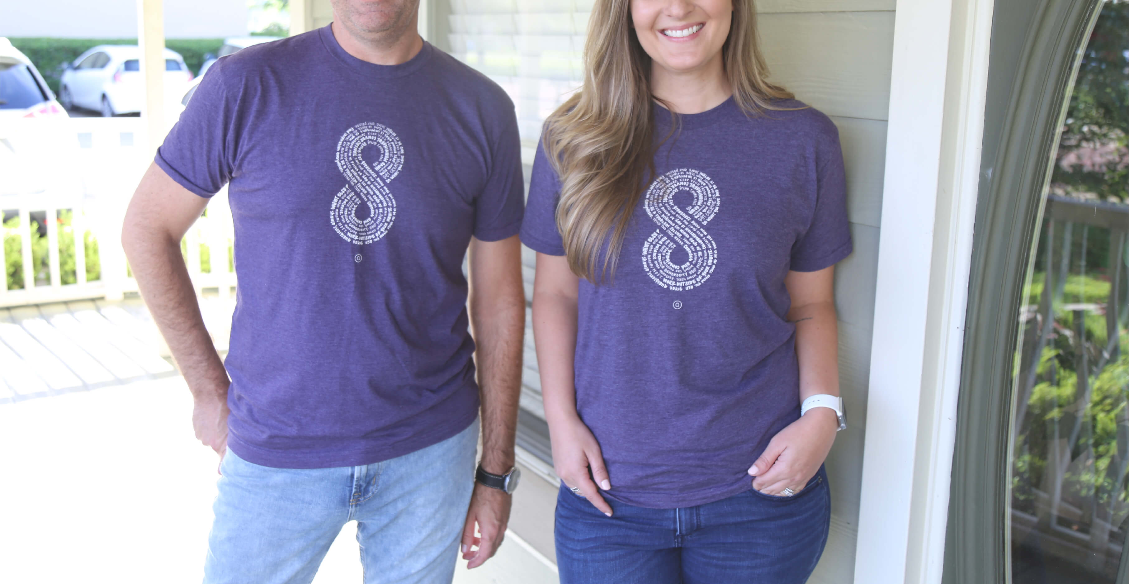 Close up of both a male and female Aedieno team member standing on a brightly lit front porch wearing purple Aedieno 8-year anniversary shirts.