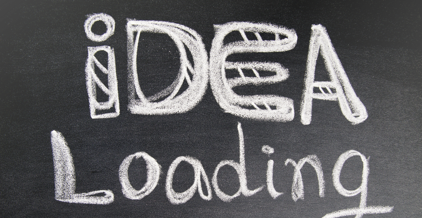 Close up of a dark gray chalkboard with decorative text in white chalk that reads: idea Loading.