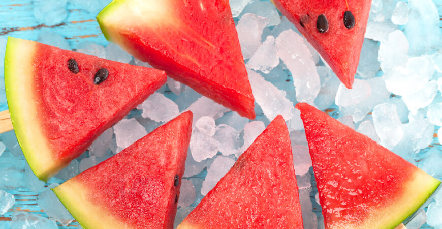 Close up of six watermelon slices sitting on ice on a blue wooden table.