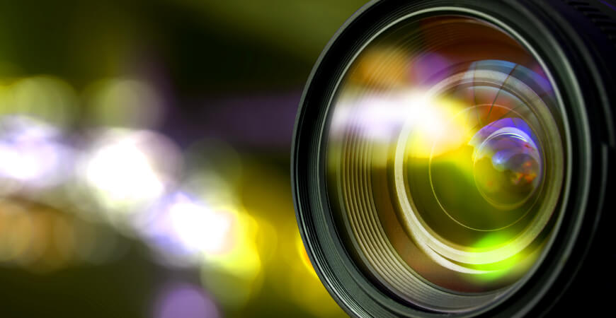 Close up of a camera lens with warm colors reflected in the glass and bokeh in the background.